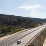 Πανοραμική άποψη αυτοκινητόδρομου με λωρίδες κυκλοφορίας, χωματόδρομους στο πλάι και αγροτική έκταση με δέντρα