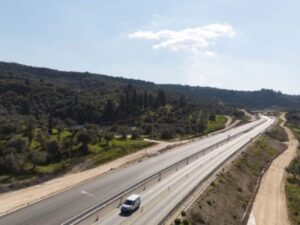 Πανοραμική άποψη αυτοκινητόδρομου με λωρίδες κυκλοφορίας, χωματόδρομους στο πλάι και αγροτική έκταση με δέντρα