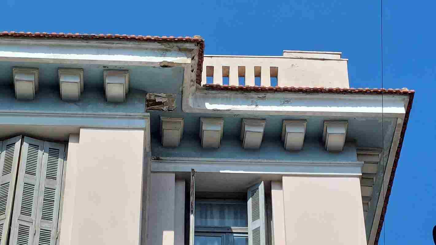 Επικίνδυνες ζημιές κτίριο, Dangerous building damage Κίνδυνος πτώσης σοβάδες, Risk of falling plaster Αποκόλληση προσόψεως, Facade detachment Συντήρηση ιστορικών κτιρίων, Historic building maintenance Φθορές νεοκλασικό κτίριο Πάτρα, Neoclassical building decay Patras Ασφάλεια πεζών κέντρο πόλης, Pedestrian safety city center Εγκατάλειψη κεντρικό κτίριο, Central building abandonment Δημόσια ασφάλεια κτίρια, Public safety buildings Γείσο κτιρίου ζημιά, Building cornice damage Αρχιτεκτονική κληρονομιά Πάτρα,