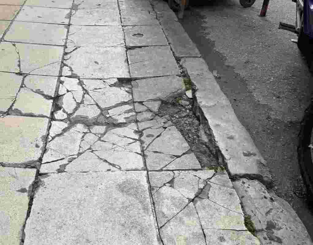 Πάτρα, Patras, οδός Πατρέως, Patreos street, κέντρο Πάτρας, Patras city center, Δήμος Πατρέων, Municipality of Patras, Αχαΐα, Achaia, Ελλάδα, Greece, πεζοδρόμιο, sidewalk, πεζοδρόμια, pavements, σπασμένες πλάκες, broken slabs, ανισοσταθμίες, uneven surfaces, κίνδυνος πεζών, pedestrian hazard, αστική υποδομή, urban infrastructure, επικίνδυνα πεζοδρόμια, dangerous sidewalks, προβλήματα υποδομών, infrastructure problems, κακοτεχνίες, poor construction work, συντήρηση δρόμων, road maintenance, ασφάλεια πεζών, pedestrian safety, κίνδυνος ατυχήματος, accident risk, τραυματισμός πεζού, pedestrian injury, άτομα με κινητικά προβλήματα, mobility impaired persons, ΑμΕΑ, PwD, δημόσια ασφάλεια, public safety, ποιότητα ζωής, quality of life, Πατρινοί, Patras citizens, διαμαρτυρία πολιτών, citizen protest, τοπικά νέα Πάτρας, Patras local news, ρεπορτάζ Πάτρα, Patras reportage, ειδήσεις Πάτρα, Patras news, Γιώργος Γιαπρακάς, Patras αυτά που δεν λέγονται