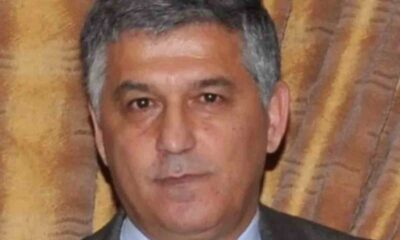 Πορτραίτο άντρα με γκριζωπά μαλλιά, ανοιχτόχρωμο πουκάμισο και σκούρο σακάκι μπροστά σε υφασμάτινο φόντο