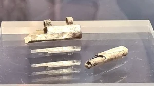 Αρχαία μεταλλική θήκη και τσαλακωμένο μεταλλικό έλασμα σε σχήμα κυλίνδρου τοποθετημένα σε επιφάνεια έκθεσης