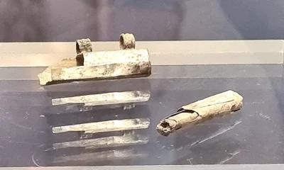 Αρχαία μεταλλική θήκη και τσαλακωμένο μεταλλικό έλασμα σε σχήμα κυλίνδρου τοποθετημένα σε επιφάνεια έκθεσης