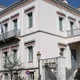 Νεοκλασικό διώροφο κτίριο με λευκή πρόσοψη, μπαλκόνια με μεταλλικά κάγκελα και ελληνικές σημαίες.