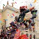 Καρναβαλικά άρματα και φιγούρες μπροστά από κτίριο υπό βροχή από χρωματιστό κομφετί.