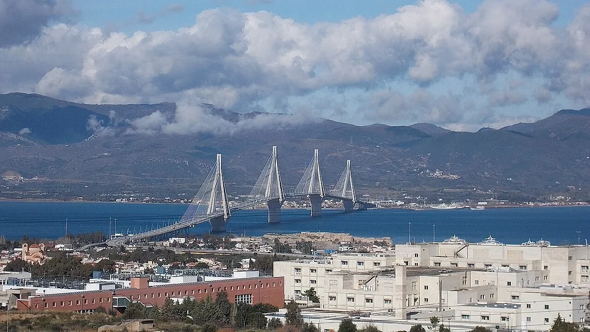Εναέρια άποψη μεγάλης καλωδιωτής γέφυρας και κτιριακού συγκροτήματος νοσοκομείου σε παράλια περιοχή με βουνά στο βάθος.