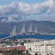 Εναέρια άποψη μεγάλης καλωδιωτής γέφυρας και κτιριακού συγκροτήματος νοσοκομείου σε παράλια περιοχή με βουνά στο βάθος.