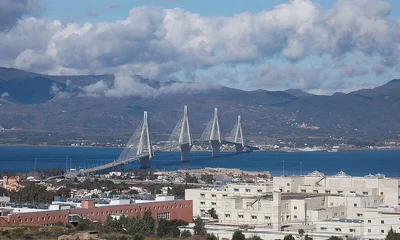 Εναέρια άποψη μεγάλης καλωδιωτής γέφυρας και κτιριακού συγκροτήματος νοσοκομείου σε παράλια περιοχή με βουνά στο βάθος.