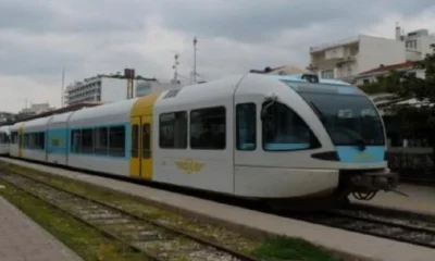 Αμαξοστοιχία του Προαστιακού σταθμευμένη σε γραμμές, με κτήρια στο βάθος.