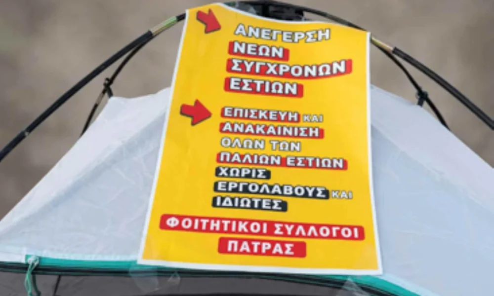 Κίτρινη ταμπέλα με συνθήματα πάνω σε σκηνή.