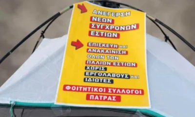 Κίτρινη ταμπέλα με συνθήματα πάνω σε σκηνή.