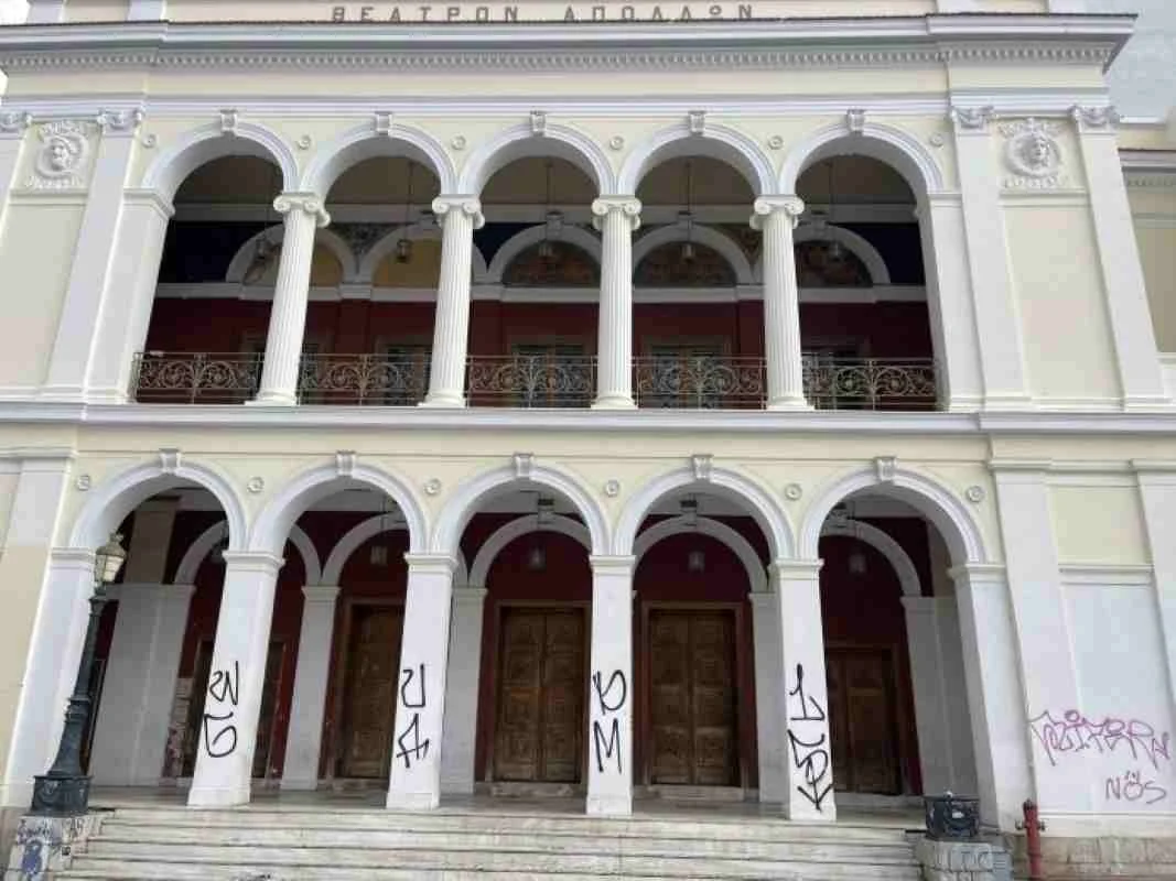 Η πρόσοψη κτιρίου με κολόνες, καμάρες, μπαλκόνι και ξύλινες πόρτες, όπου διακρίνονται συνθήματα σε λευκές κολόνες.