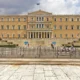 Το κτίριο της Βουλής των Ελλήνων στην Αθήνα, μπροστά από το οποίοι υπάρχουν προστατευτικά κιγκλιδώματα και περαστικοί.