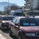 Σειρά από σταθμευμένα αυτοκίνητα ταξί σε δρόμο πόλης με κίνηση και κτίρια στο βάθος.