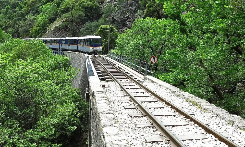 Συρμός τρένου κινείται σε γεφύρι πάνω από σιδηροδρομική γραμμή σε ορεινή δασική περιοχή