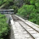 Συρμός τρένου κινείται σε γεφύρι πάνω από σιδηροδρομική γραμμή σε ορεινή δασική περιοχή