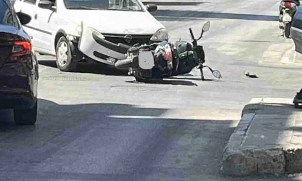 Πτώση δικύκλου στο οδόστρωμα κοντά σε λευκό αυτοκίνητο σε δρόμο.
