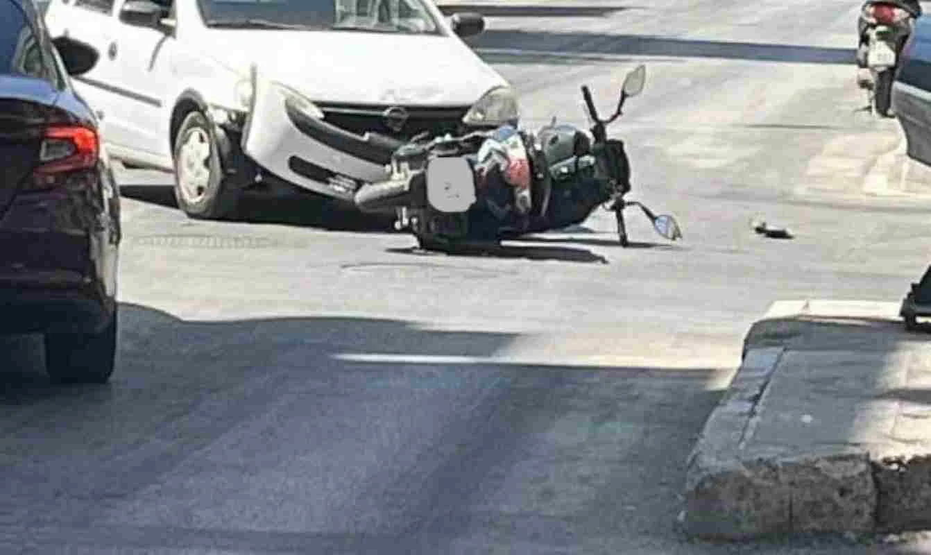 Πτώση δικύκλου στο οδόστρωμα κοντά σε λευκό αυτοκίνητο σε δρόμο.