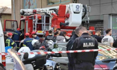 Πλήθος κόσμου και αστυνομικοί συγκεντρωμένοι σε δρόμο μπροστά από όχημα της πυροσβεστικής και αυτοκίνητα, αποκλεισμένοι με κόκκινη