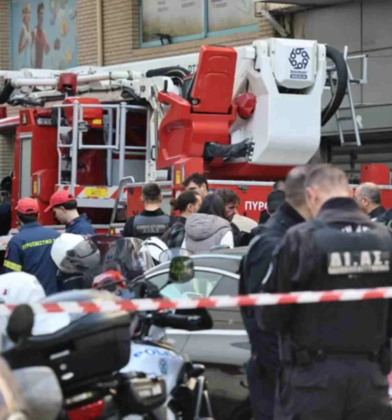 Πλήθος κόσμου και αστυνομικοί συγκεντρωμένοι σε δρόμο μπροστά από όχημα της πυροσβεστικής και αυτοκίνητα, αποκλεισμένοι με κόκκινη