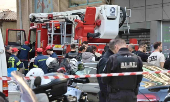 Πλήθος κόσμου και αστυνομικοί συγκεντρωμένοι σε δρόμο μπροστά από όχημα της πυροσβεστικής και αυτοκίνητα, αποκλεισμένοι με κόκκινη