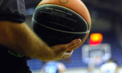Χέρι κρατάει μπάλα μπάσκετ σε γήπεδο με θολό φόντο.