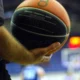 Χέρι κρατάει μπάλα μπάσκετ σε γήπεδο με θολό φόντο.