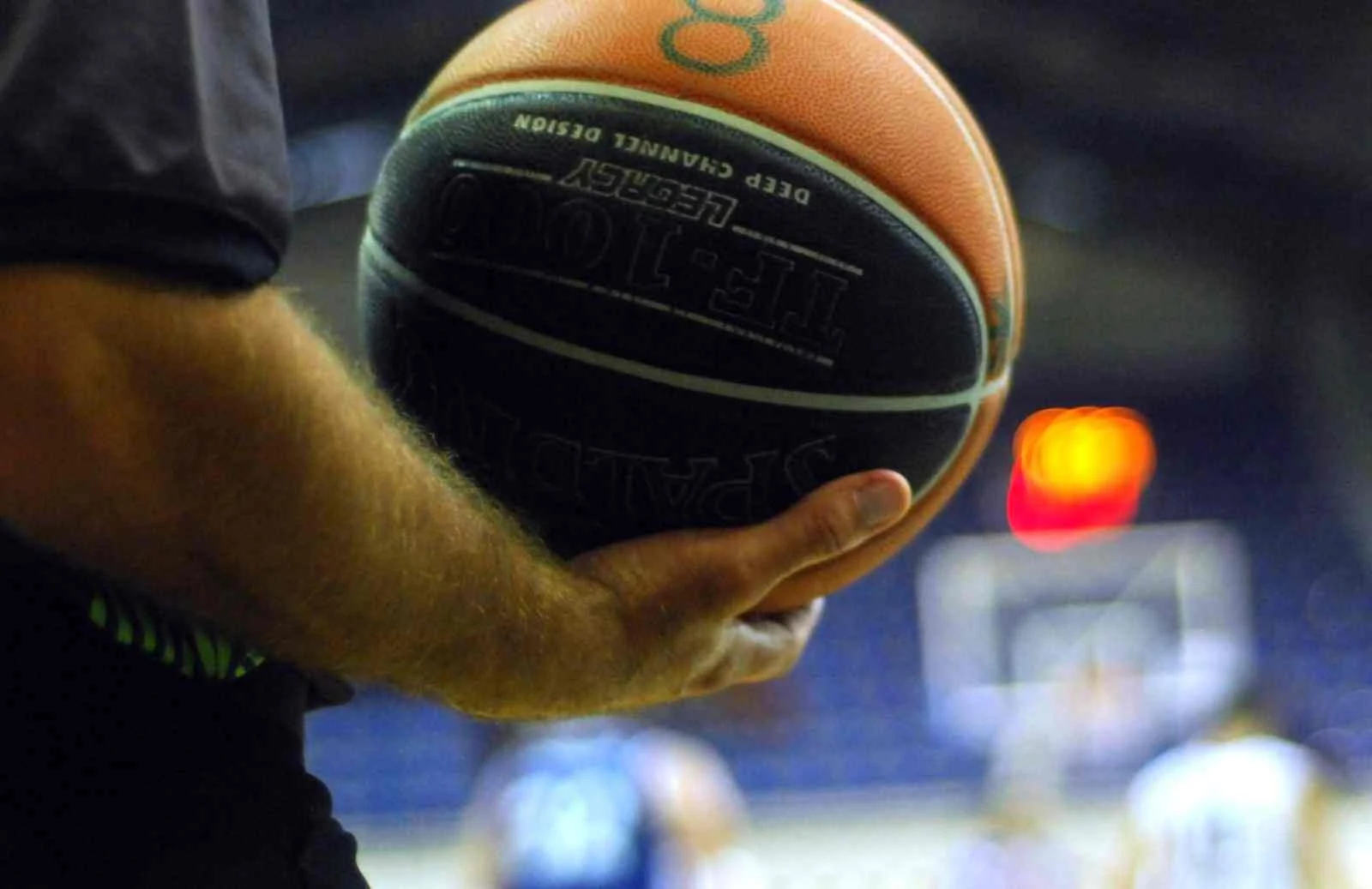 Χέρι κρατάει μπάλα μπάσκετ σε γήπεδο με θολό φόντο.