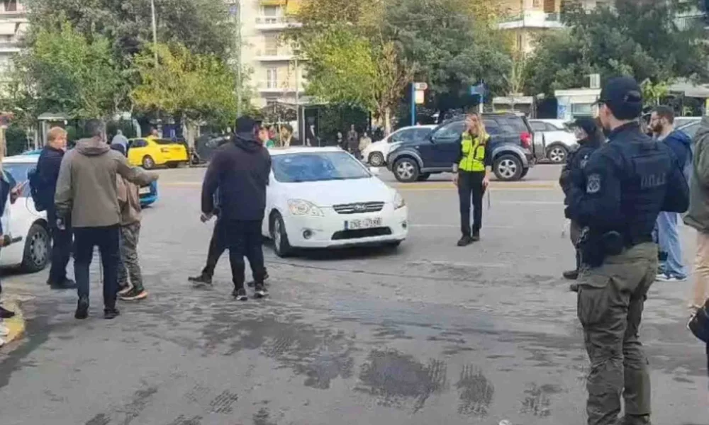 Άτομα και αστυνομικοί σε δρόμο με αυτοκίνητα και κτίρια στο βάθος