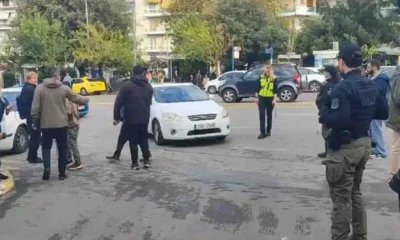 Άτομα και αστυνομικοί σε δρόμο με αυτοκίνητα και κτίρια στο βάθος