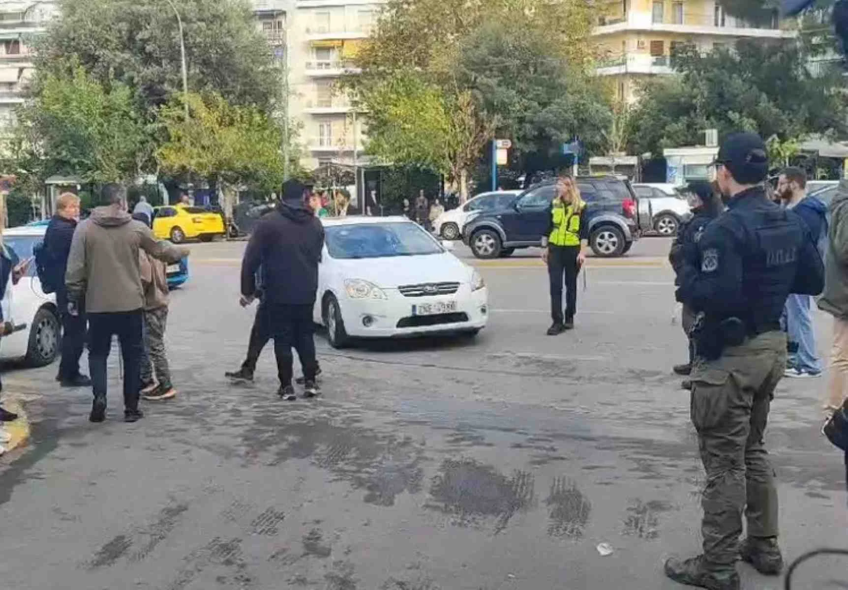 Άτομα και αστυνομικοί σε δρόμο με αυτοκίνητα και κτίρια στο βάθος