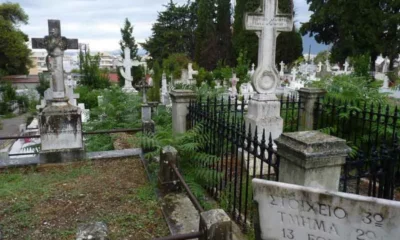 Άποψη νεκροταφείου με μαρμάρινους σταυρούς, τάφους, μεταλλικό φράχτη και επιγραφή σε μαρμάρινη στήλη