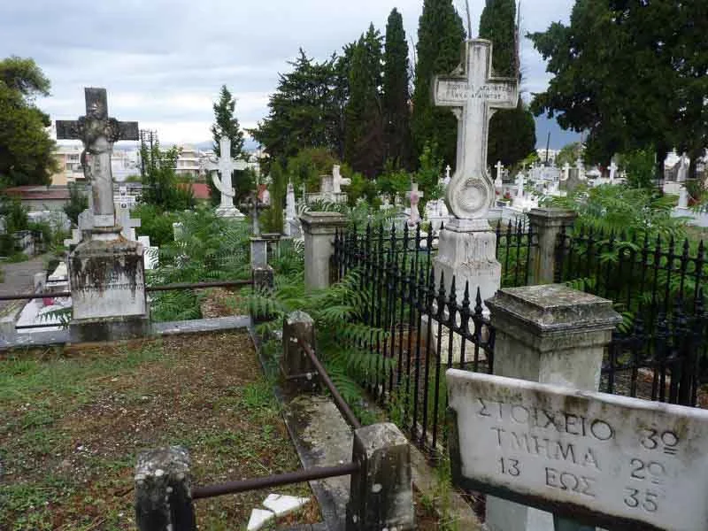 Άποψη νεκροταφείου με μαρμάρινους σταυρούς, τάφους, μεταλλικό φράχτη και επιγραφή σε μαρμάρινη στήλη