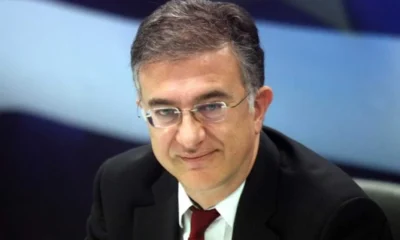 Άντρας με γυαλιά οράσεως, κοστούμι και κόκκινη γραβάτα κοιτάζει μπροστά.