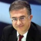 Άντρας με γυαλιά οράσεως, κοστούμι και κόκκινη γραβάτα κοιτάζει μπροστά.