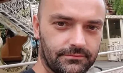 Πορτραίτο άνδρα με κοντά μαλλιά και μούσι, ο οποίος φοράει σκούρο μπλουζάκι σε εξωτερικό χώρο.