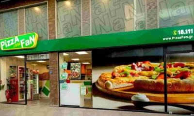 Πρόσοψη καταστήματος με επιγραφή Pizza Fan και μεγάλη φωτογραφία πίτσας στη τζαμαρία