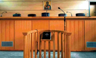 Ξύλινο εδώλιο δικαστηρίου με μικρόφωνα και θρησκευτική εικόνα στον τοίχο