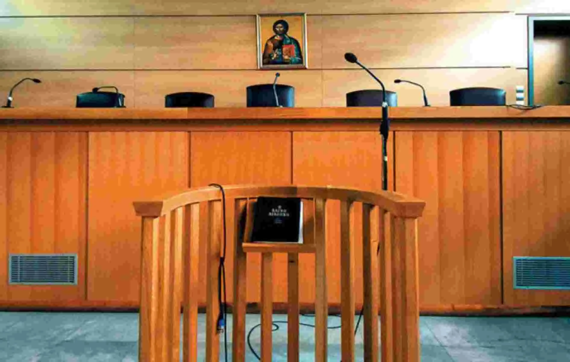 Ξύλινο εδώλιο δικαστηρίου με μικρόφωνα και θρησκευτική εικόνα στον τοίχο