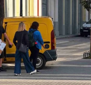 Άτομα κινούνται σε πεζοδρόμηση δίπλα από σταθμευμένο κίτρινο βαν