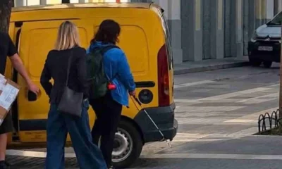 Άτομα κινούνται σε πεζοδρόμηση δίπλα από σταθμευμένο κίτρινο βαν
