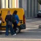 Άτομα κινούνται σε πεζοδρόμηση δίπλα από σταθμευμένο κίτρινο βαν