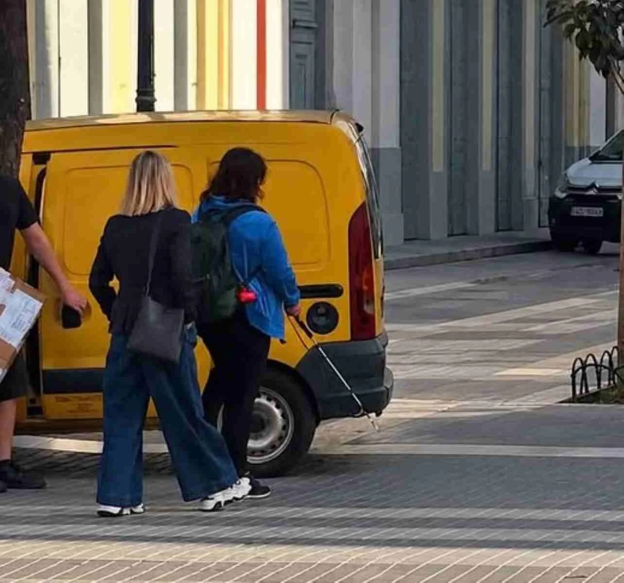 Άτομα κινούνται σε πεζοδρόμηση δίπλα από σταθμευμένο κίτρινο βαν