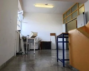 Εσωτερικός χώρος κτιρίου με ανοιχτό παράθυρο, έπιπλα, ηλεκτρονικό εξοπλισμό και αποθηκευμένα αντικείμενα στο πάτωμα.
