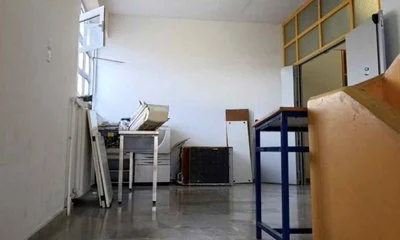 Εσωτερικός χώρος κτιρίου με ανοιχτό παράθυρο, έπιπλα, ηλεκτρονικό εξοπλισμό και αποθηκευμένα αντικείμενα στο πάτωμα.