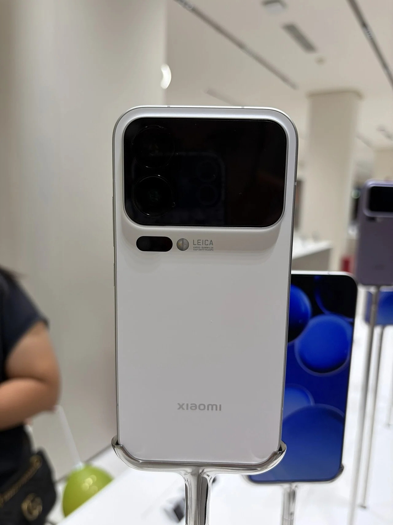 Πίσω όψη λευκού smartphone σε βάθρο έκθεσης, με διπλή οθόνη και κάμερες