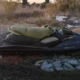 Εγκαταλελειμμένο θαλάσσιο όχημα τύπου τζετ σκι σε υπαίθριο χώρο με πέτρες και ξερά χόρτα.