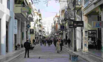 Άποψη πολυσύχναστου εμπορικού δρόμου ανάμεσα σε κτήρια με καταστήματα και πεζούς.