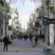 Άποψη πολυσύχναστου εμπορικού δρόμου ανάμεσα σε κτήρια με καταστήματα και πεζούς.