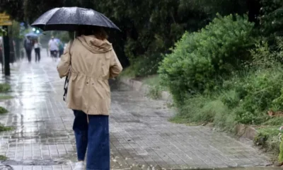 Άτομο με ομπρέλα και αδιάβροχο περπατά σε βρεγμένο πεζοδρόμιο υπό βροχή